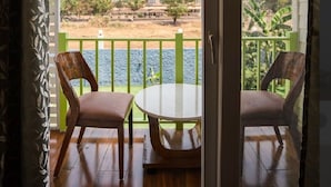 Varanda com duas cadeiras de madeira e uma mesa, com vista para um corpo de água e vegetação.