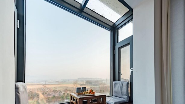 A room with a large window, a wooden table with a cup and fruits, and a magazine on the floor. - zz's hotel (Haikou)