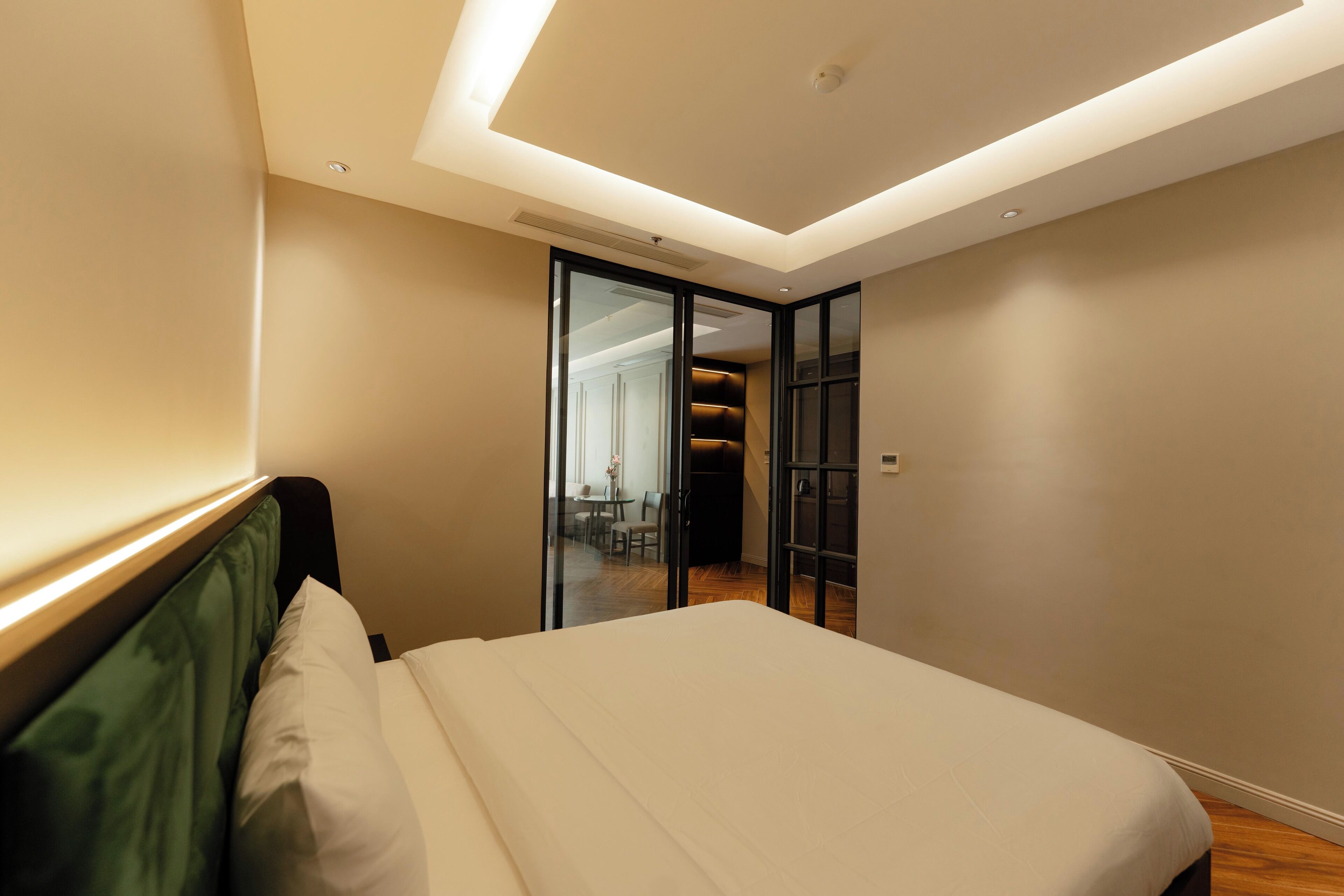 A modern bedroom with a bed, a green headboard, and a glass door leading to a dining area.