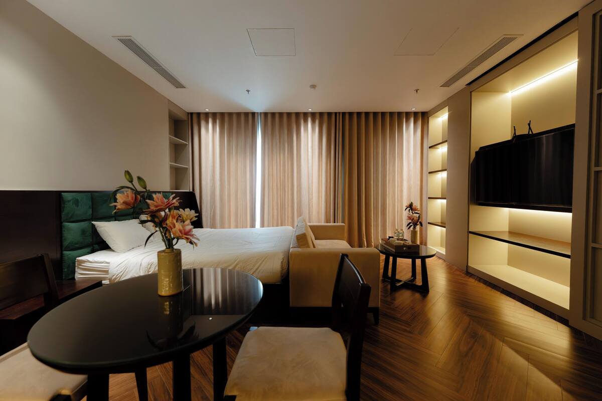 Habitación de hotel con cama, escritorio, silla, mesita, televisor y cortina.