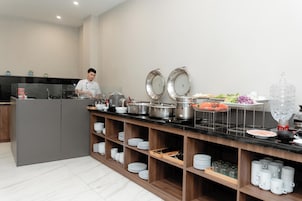 Una cocina moderna con un chef preparando comida, equipada con electrodomésticos de acero inoxidable, repisas de madera con platos y una variedad de alimentos.