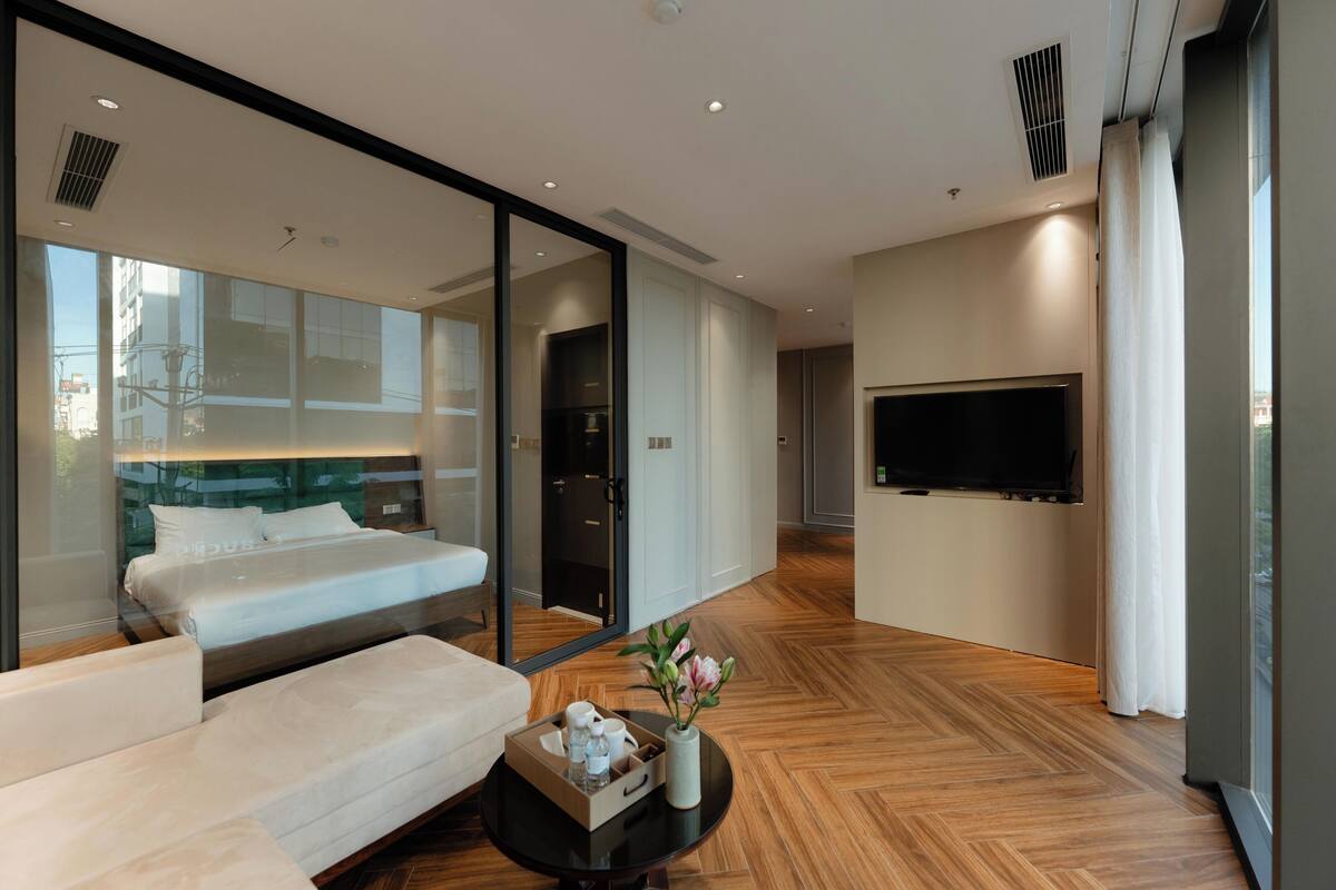 Habitación de hotel moderna con una cama grande, un sofá, un televisor montado en la pared y suelo de madera.