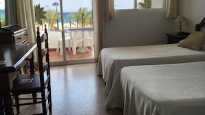Une chambre d’hôtel avec deux lits, un bureau et vue sur la plage.
