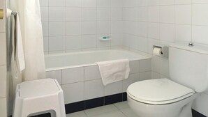 Une salle de bain avec une baignoire blanche, des toilettes et un petit tabouret.