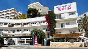 Un immeuble à plusieurs étages doté de balcons, d’une enseigne bien visible indiquant « APARTAMENTOS BAHIA », et d’un espace extérieur couvert avec un mur en pierre.