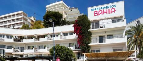 A multi-story building with balconies, a prominent sign reading "APARTAMENTOS BAHIA," and a covered outdoor area with a stone wall.