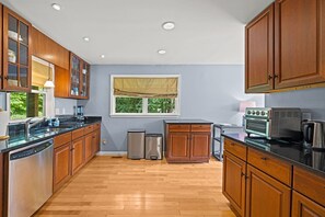 A kitchen with wooden cabinets, a window with a view, a dishwasher, a trash can, and a vintage oven. - Riverfront Cabin Getaway with Fire Pit! (Harpers Ferry)