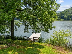 A lakeside picnic area with a wooden bench and table, surrounded by lush greenery and a clear view of the lake. - Riverfront Cabin Getaway with Fire Pit! (Harpers Ferry)
