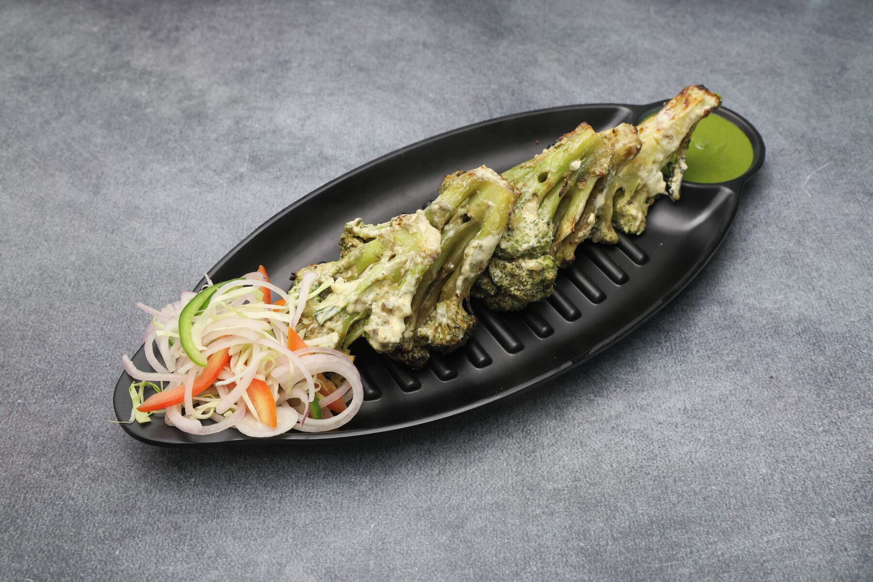 A black plate with grilled vegetables and a side salad.