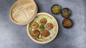 Un panier vapeur en bambou contenant des raviolis et trois petits bols de sauces.