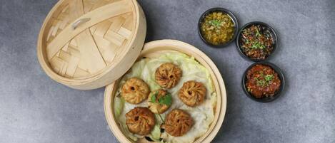 A bamboo steamer with dumplings and three small bowls of sauces.