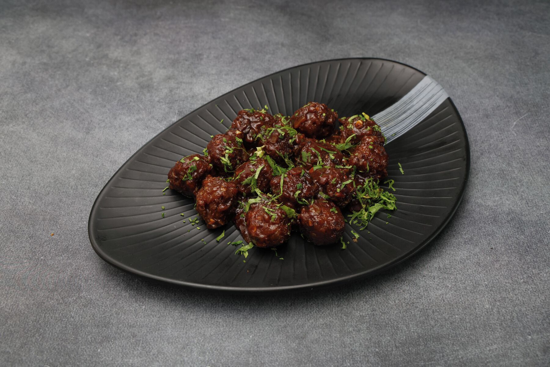 A dark plate with meatballs garnished with green herbs.