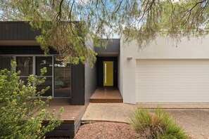 A modern house with a wooden deck, a garage, and a yellow door. - Stardust Sands by Ready Set Stay (Cowes)