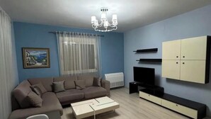 A modern living room with a sectional sofa, a dining table, and a TV mounted on the wall. - Nice an calm Apartment in Tirana City (Tiranë)