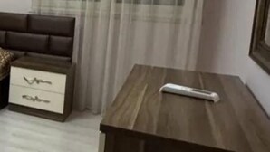 A bedroom with a bed, a nightstand with drawers, a wooden side table, and a window with sheer curtains. - Nice an calm Apartment in Tirana City (Tiranë)