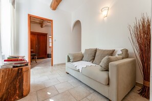 Un soggiorno con un divano, un tavolino in legno, una libreria, un lampadario a parete e una porta che dà su un'altra stanza.