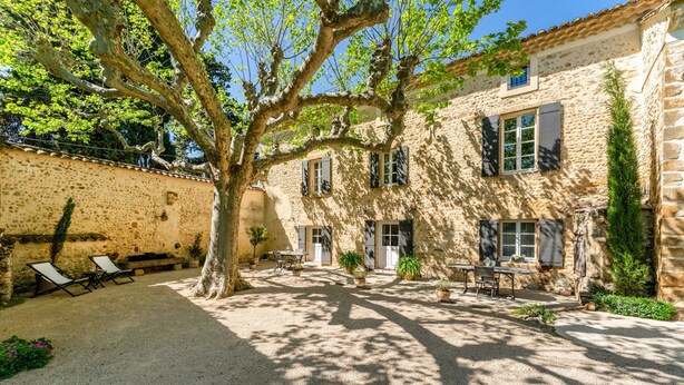 Une cour avec un bâtiment en pierre, des sièges en plein air et des plantes en pot.
