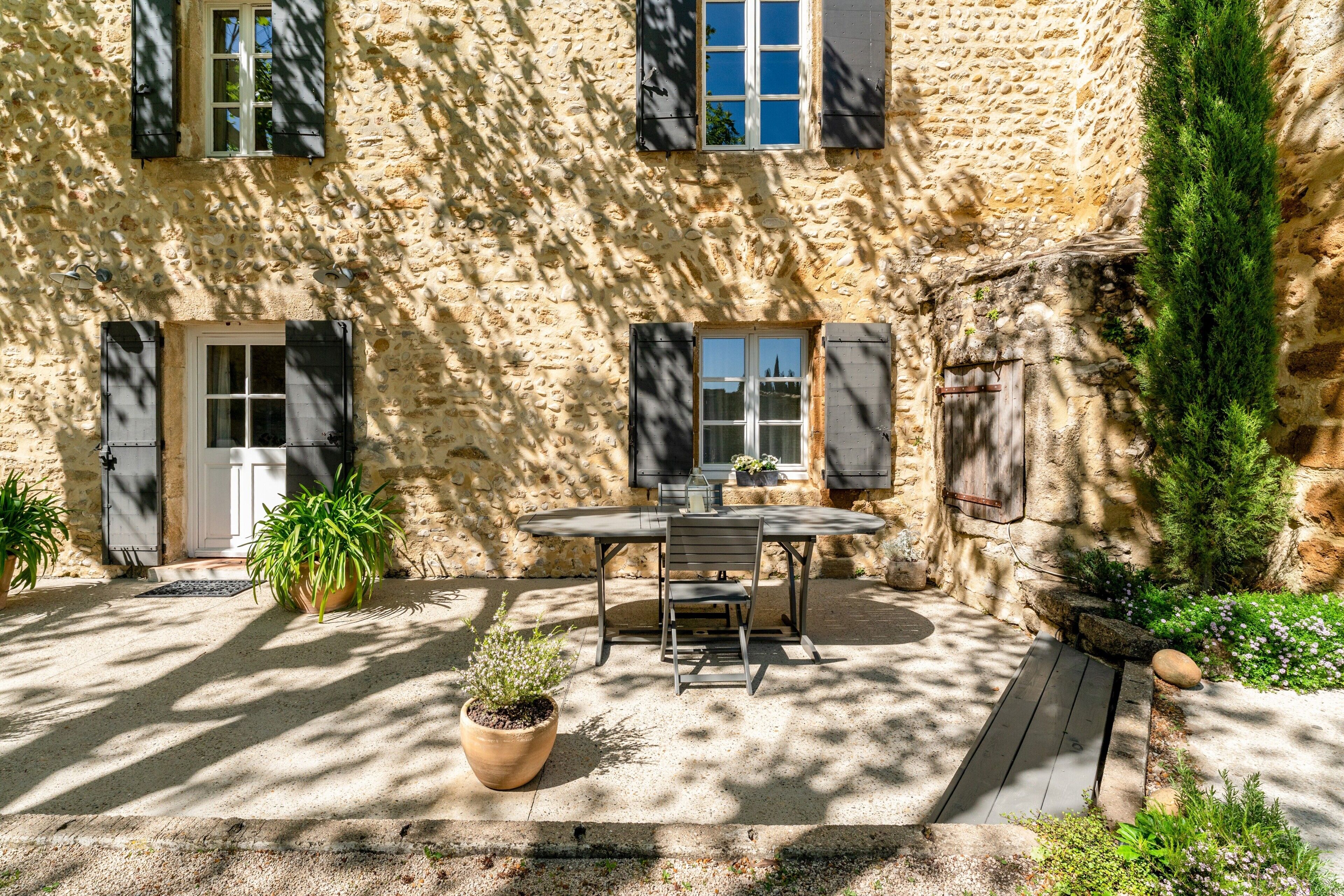 Un edificio de piedra con un patio, una mesa con sillas y plantas en macetas.