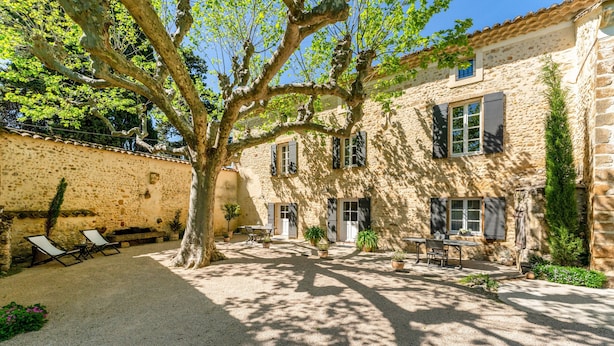 A courtyard with a stone building, outdoor seating, and potted plants.
