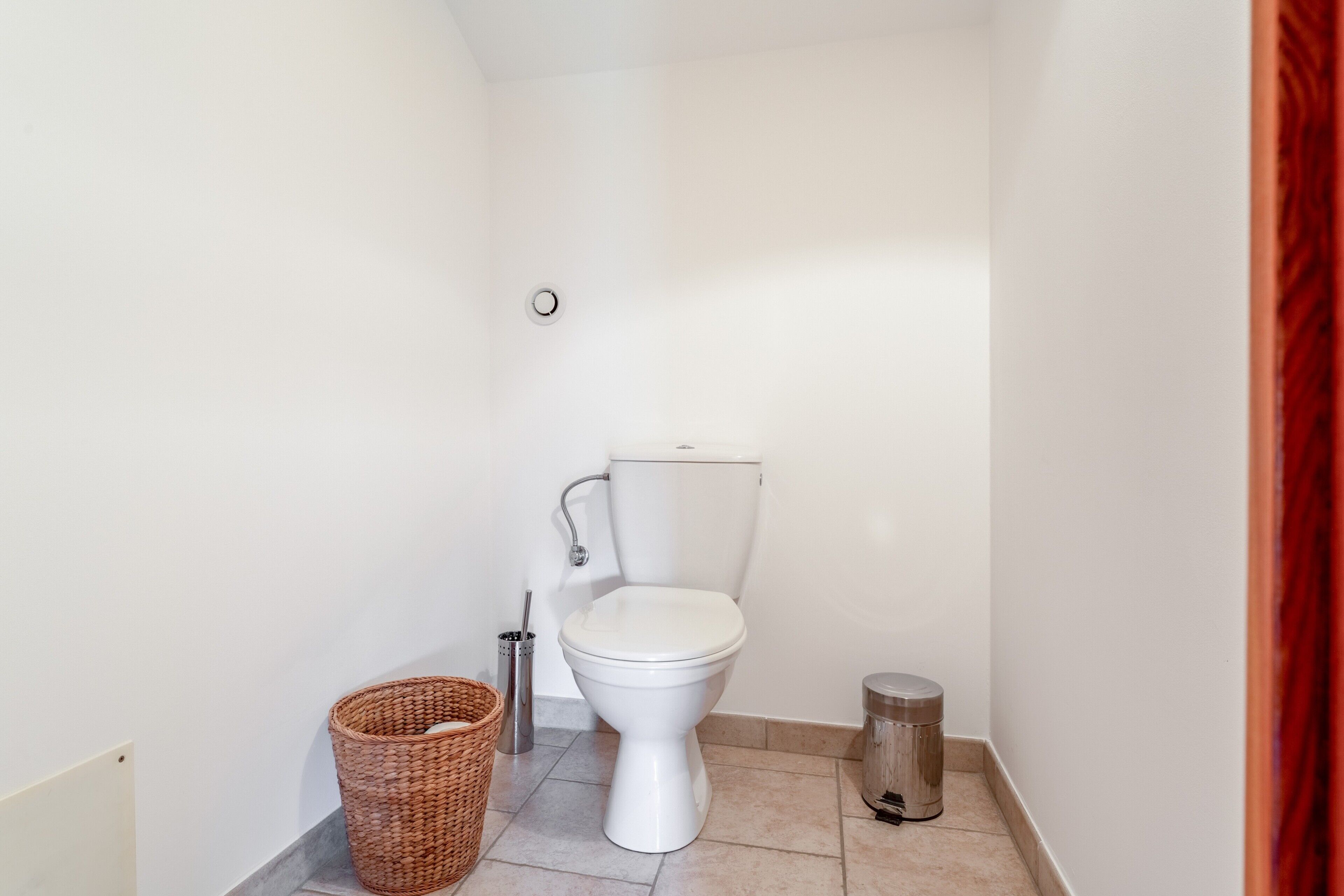 Une petite salle de bain blanche, avec des toilettes, une poubelle et un panier en osier.
