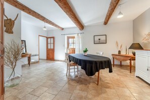 Un coin repas comprenant une table, des chaises, une plante en pot, un meuble en bois et un plafond rustique.