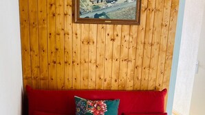 Um sofá vermelho com almofadas florais, encostado a uma parede de madeira com um quadro emoldurado acima.