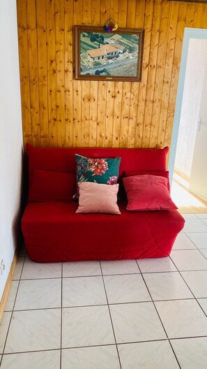 A red sofa with floral cushions against a wooden wall with a framed picture above. - Quiet apartment 75 M2 2 bedrooms near ski lifts resort center (Huez)