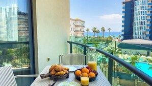A balcony with breakfast items, a view of a pool, and surrounding buildings. - Apartment 1+1 Qoople Excellence B19 100 m from the sea (Alanya)
