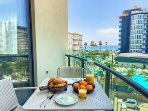 A balcony with breakfast items, a view of a pool, and surrounding buildings. - Apartment 1+1 Qoople Excellence B19 100 m from the sea (Alanya)