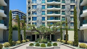 A modern building with multiple balconies, a central courtyard with trees, and a clear sky. - Apartment 1+1 Qoople Excellence B19 100 m from the sea (Alanya)