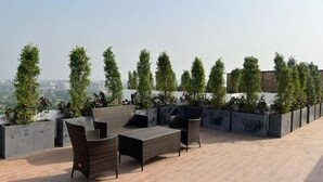 Une terrasse sur le toit, meublée de mobilier en osier, offrant une vue sur la ville et bordée d’une rangée d’arbres.