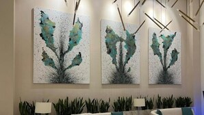 Un salon moderne avec des canapés blancs, une table basse et trois tableaux abstraits accrochés au mur.