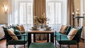 A dining area with a table set for two, flanked by two green upholstered chairs with patterned cushions. A vase with dried flowers is on the table, and a candle holder with candles is to the right. - Boutique hotel Soukeníkův dům (Kutna Hora)