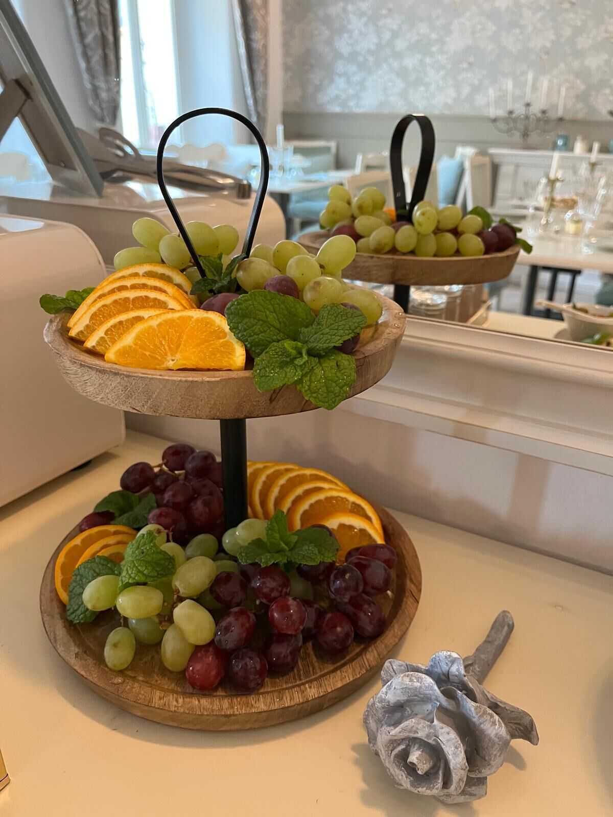 A two-tiered fruit platter with grapes and orange slices, set on a table in a dining area.