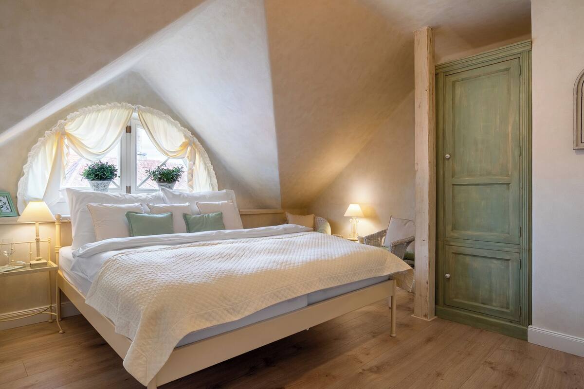Ein Schlafzimmer mit einem Bett, einem Fenster mit Vorhängen, einer Tür und Nachttischlampen.