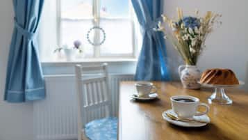 A dining table with two cups of coffee, a cake on a stand, and a vase of flowers.