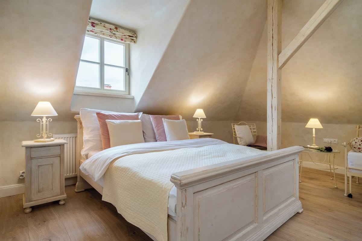 Ein Schlafzimmer mit einem großen Bett, zwei Nachttischen mit Lampen, einem Fenster und einer geneigten Decke.