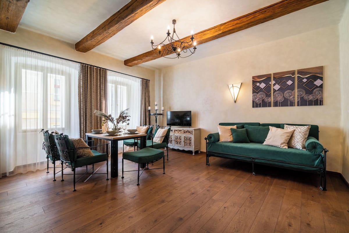Ein Wohnzimmer mit Holzboden, einem grünen Sofa, einem Esstisch mit Stühlen und einem Fernseher auf einem Schrank.