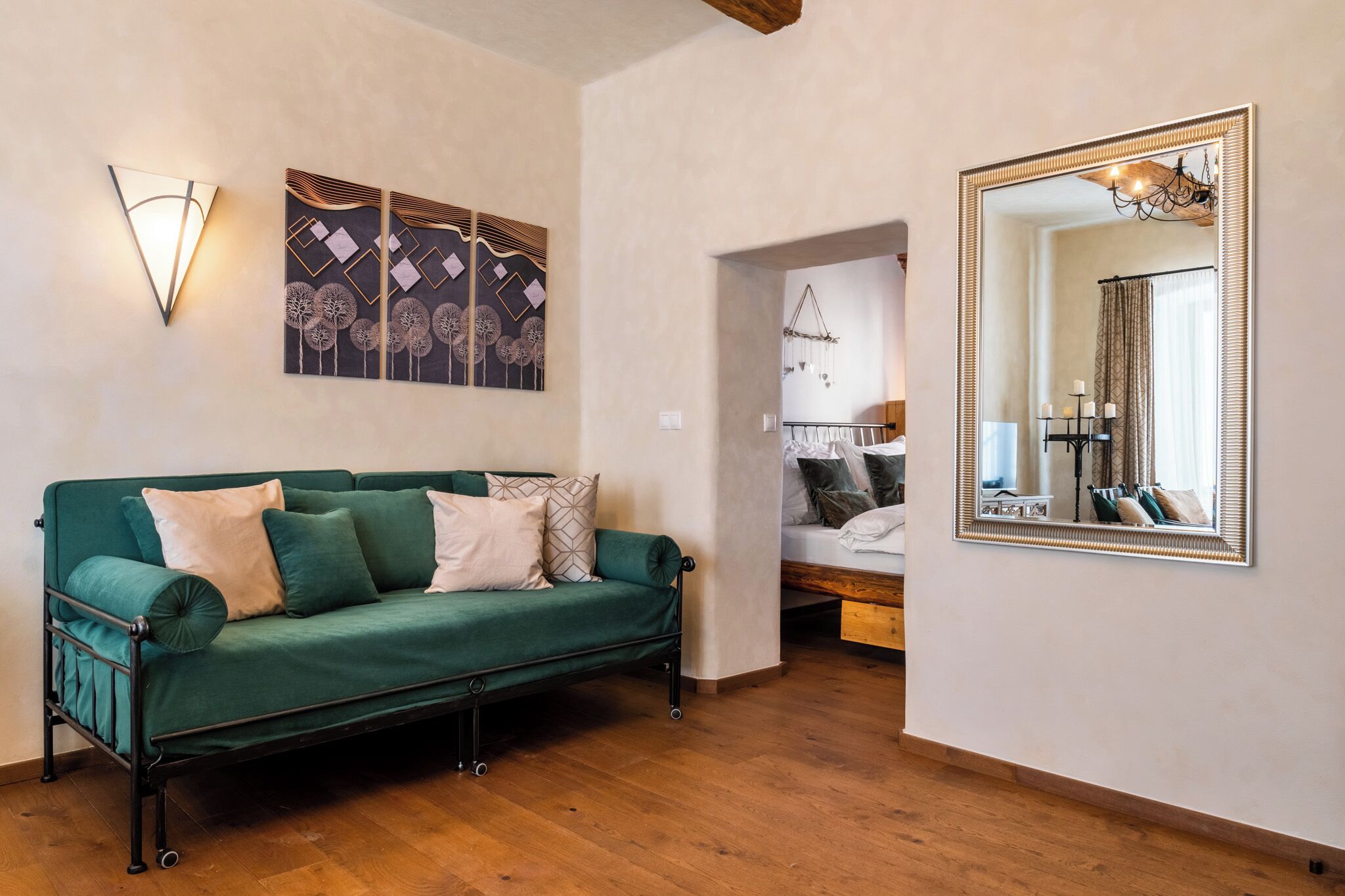 Una habitación con un sofá verde, un espejo grande y decoración en la pared.