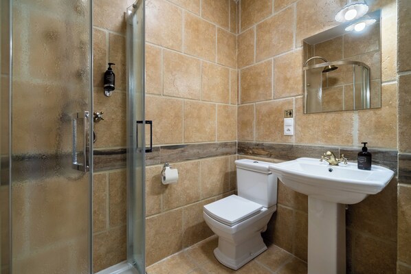 Un baño con cabina de ducha de vidrio, inodoro y lavamanos pedestal.