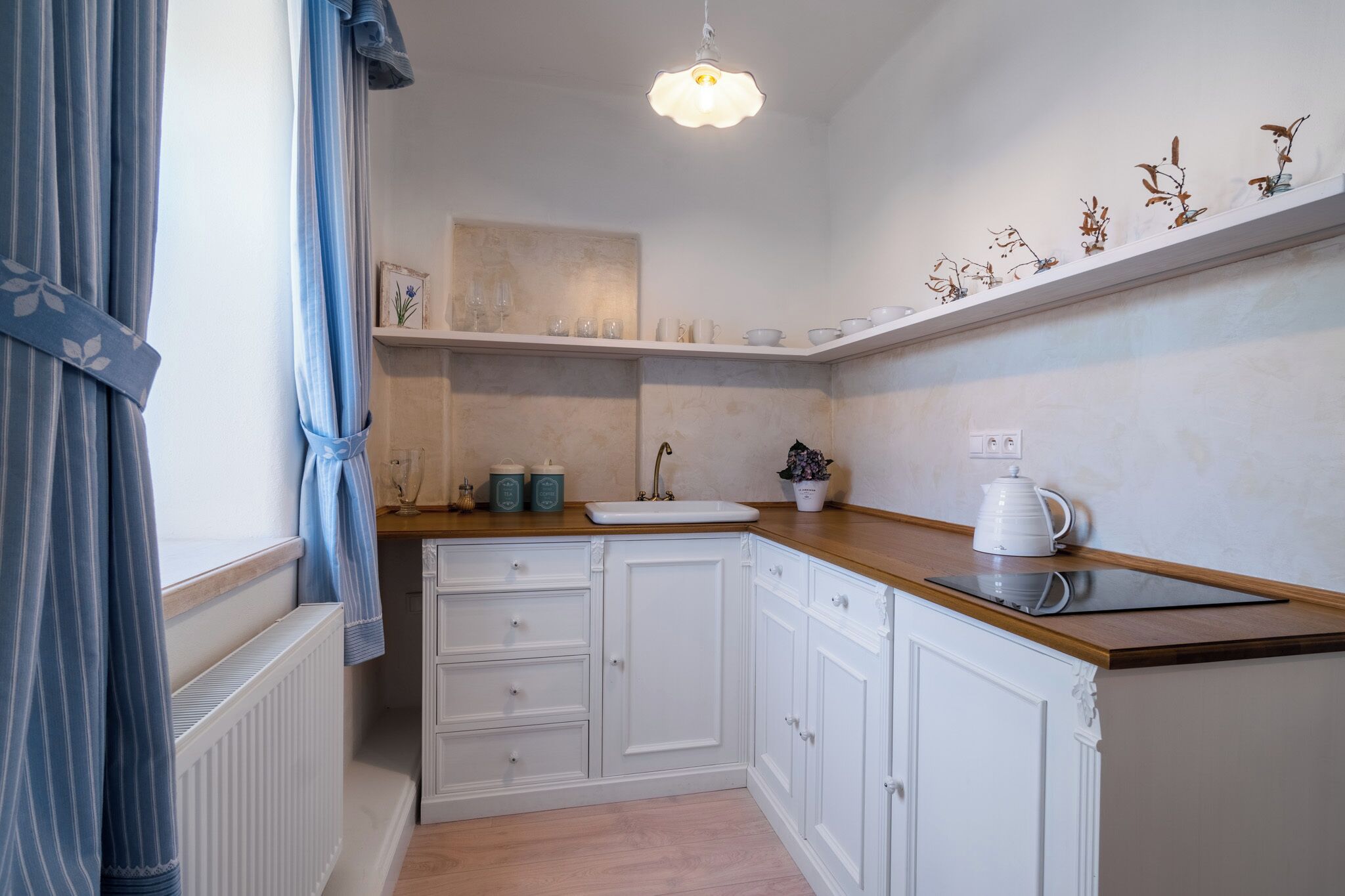Une cuisine moderne avec des meubles blancs, un plan de travail en bois et un évier blanc. Une étagère contenant des objets décoratifs se trouve au-dessus de l’évier.