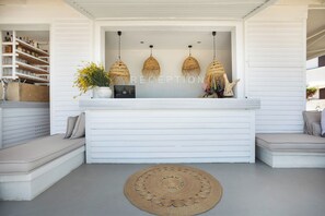 A reception area with a white counter, three woven pendant lights, a reception desk, and a round woven rug. - Adriana Beach (Pefkochori)