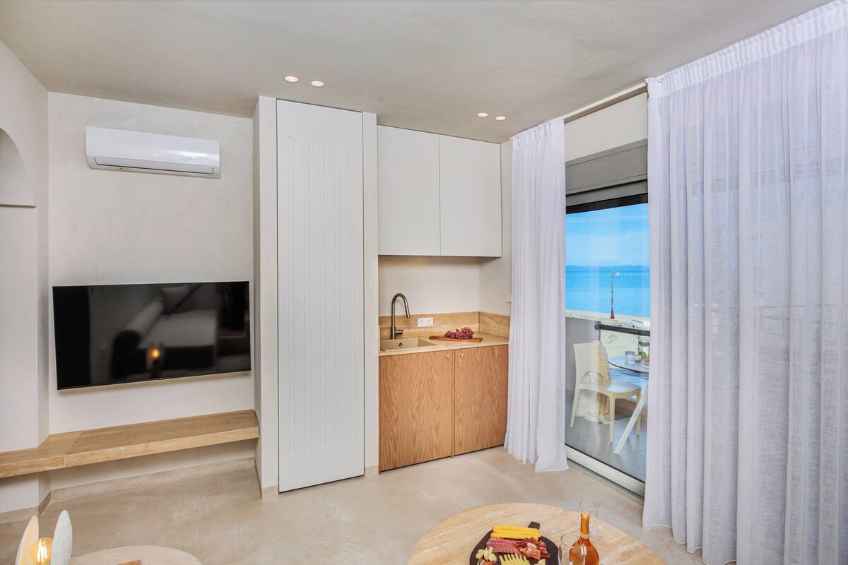 A modern kitchen with a TV, wooden cabinets, and a view of the sea.