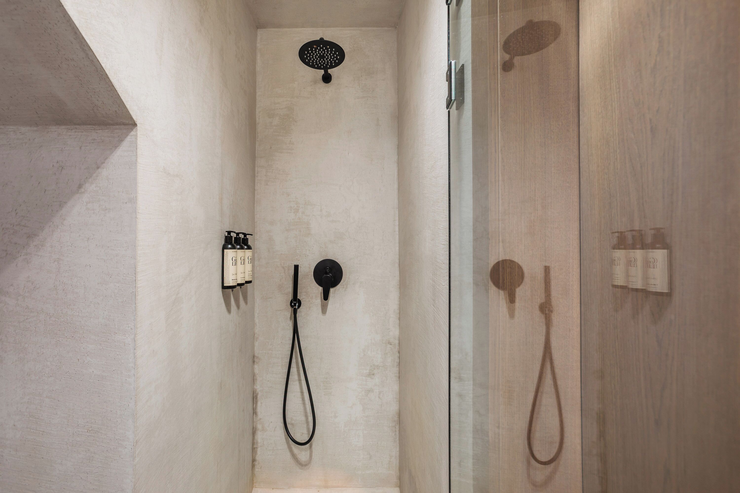 A shower with a handheld showerhead, a wall-mounted control panel, and a glass partition.