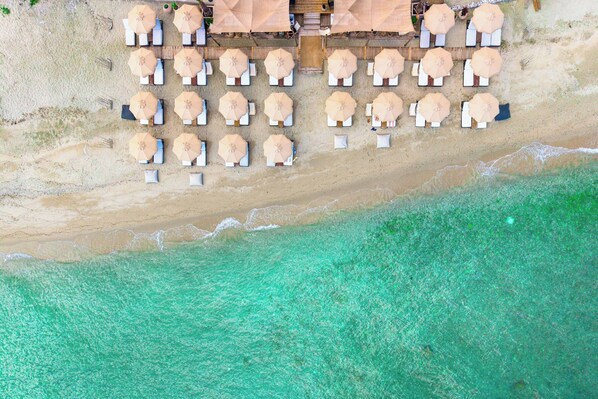 An aerial view of a beach with rows of sun loungers and umbrellas, a wooden walkway, and clear turquoise waters. - Adriana Beach (Pefkochori)