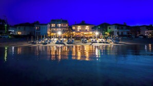 A beachfront hotel with a pool, multiple lounge chairs, and a well-lit building. - Adriana Beach (Pefkochori)