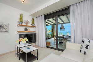 Una sala de estar moderna con un sofá, una mesa de centro, un televisor y un balcón con vistas al mar.