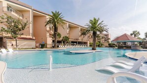 Una piscina con sillas de descanso, palmeras y un edificio con balcones al fondo.