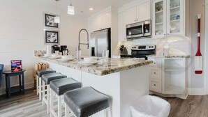Una cocina moderna con armarios blancos, encimera de mármol y refrigerador de acero inoxidable.
