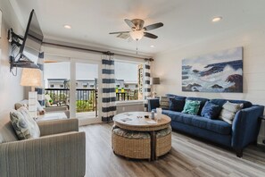 A living room with a blue sofa, a round wicker coffee table, and a ceiling fan. - Ocean Vista Three -Things Are Better in 3's (Galveston)